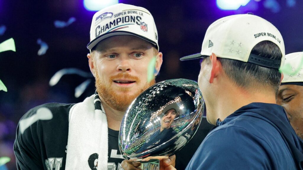 El coach Mike Macdonald le entrega el trofeo a Sam Darnold. Reuters 